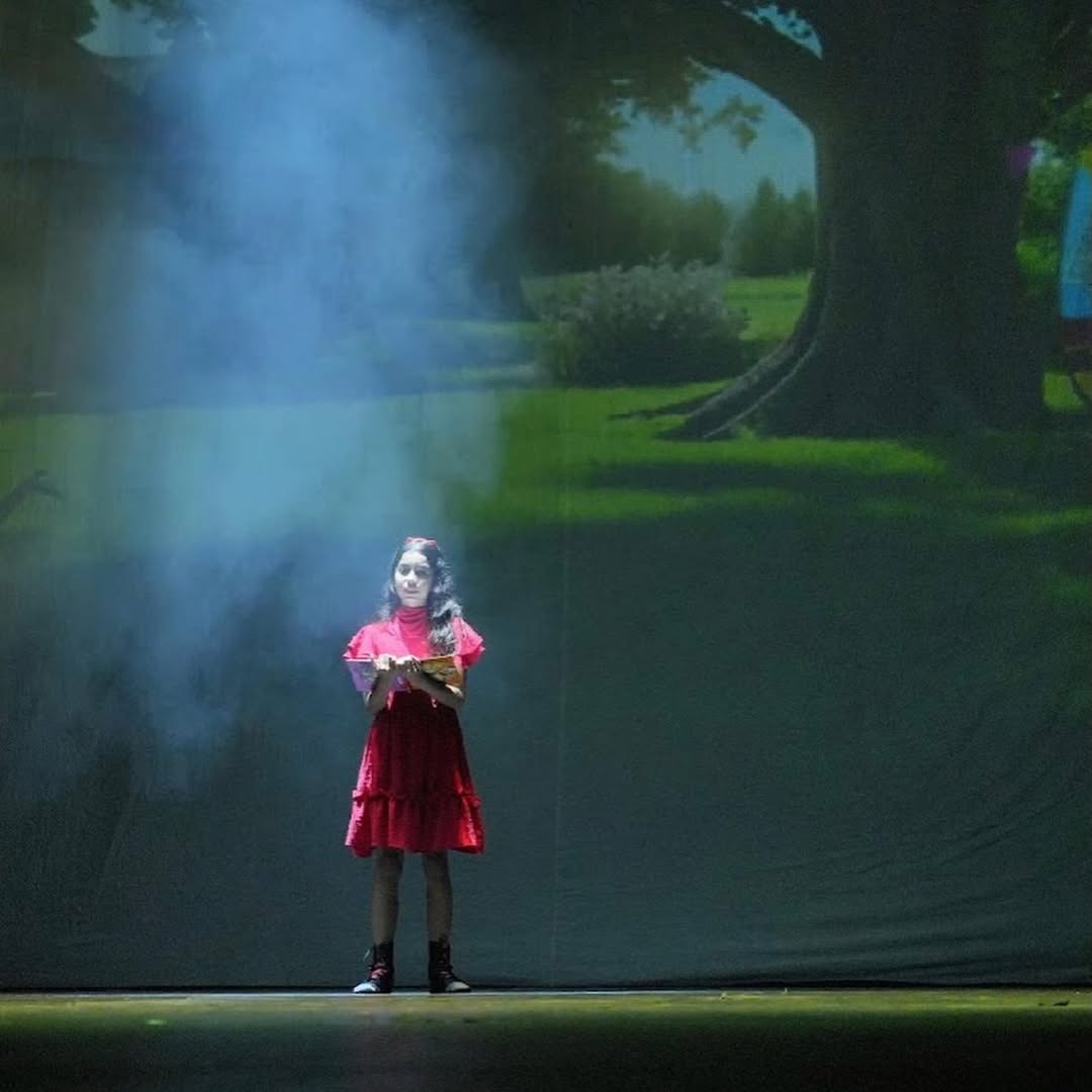 Matilda em cena com seu livro no vestido vermelho