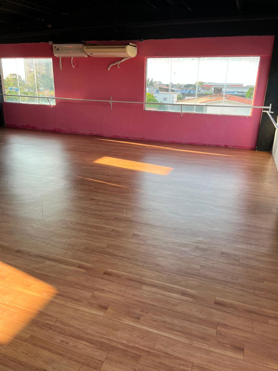 Estúdio de dança do NED com janelas amplas, parede rosa e vista para o bairro