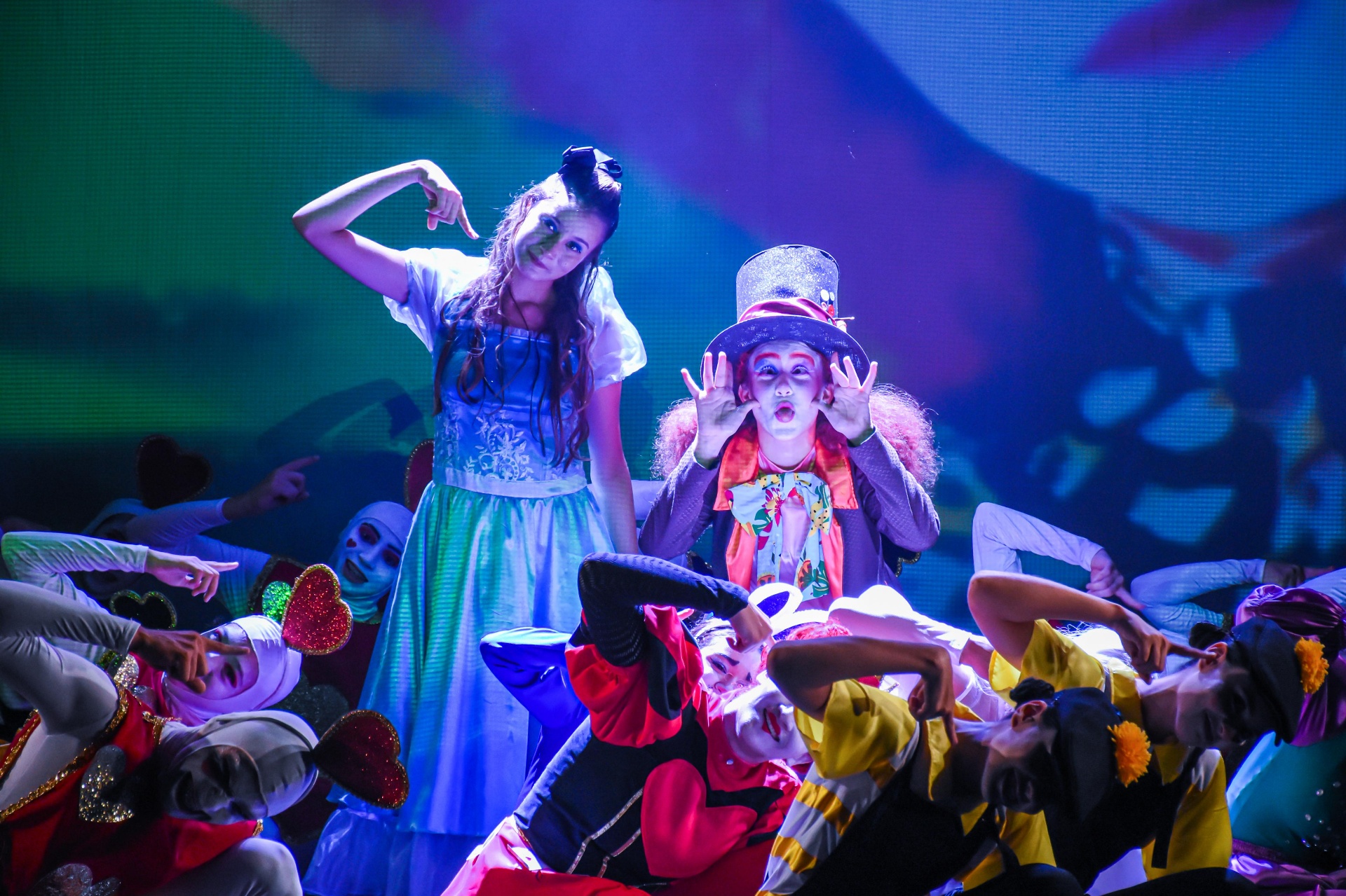 Chapeleiro e Alice em cena cercados por personagens do País das Maravilhas