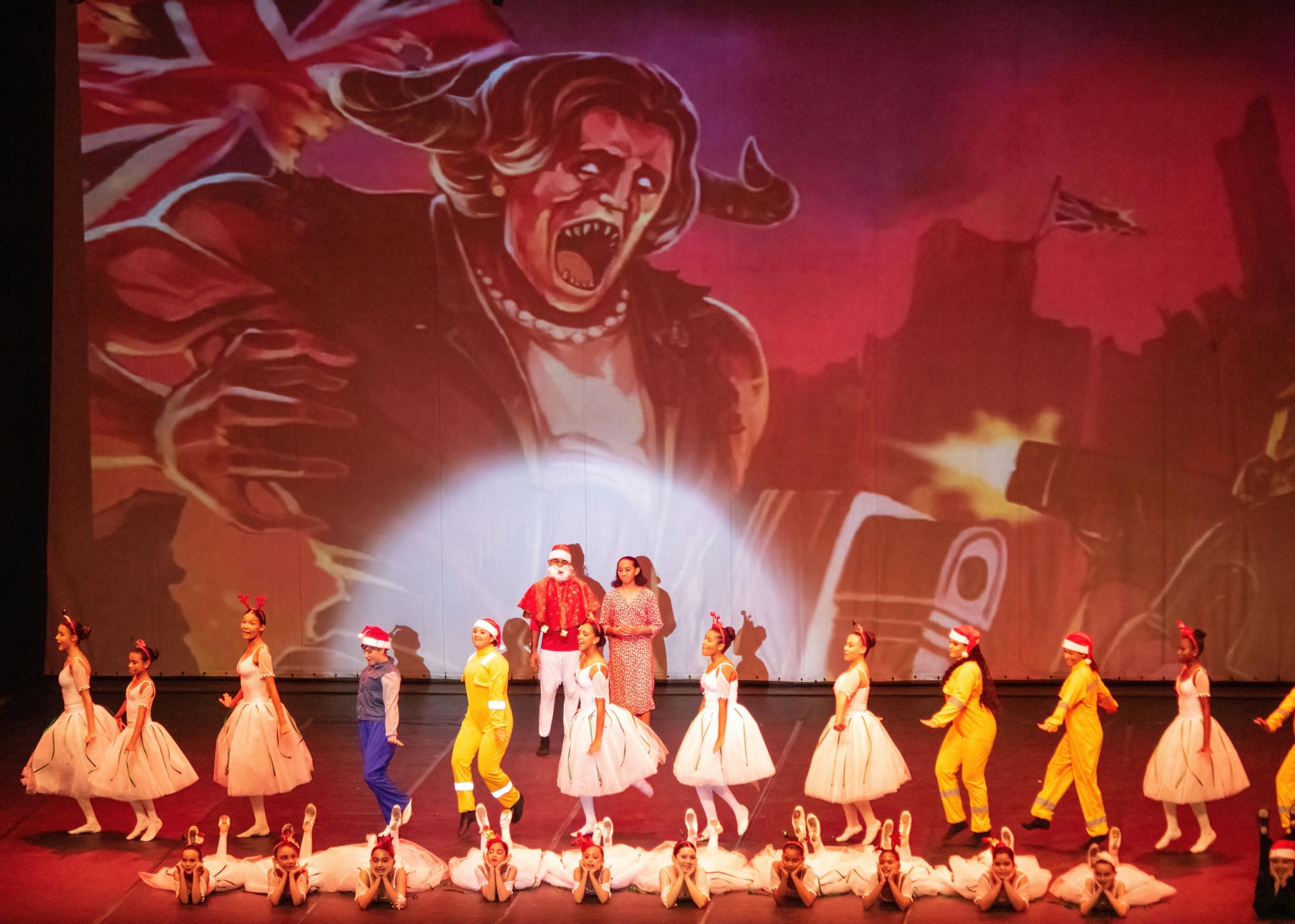 Projeção da Thatcher ao fundo enquanto elenco natalino se apresenta no Billy Elliot
