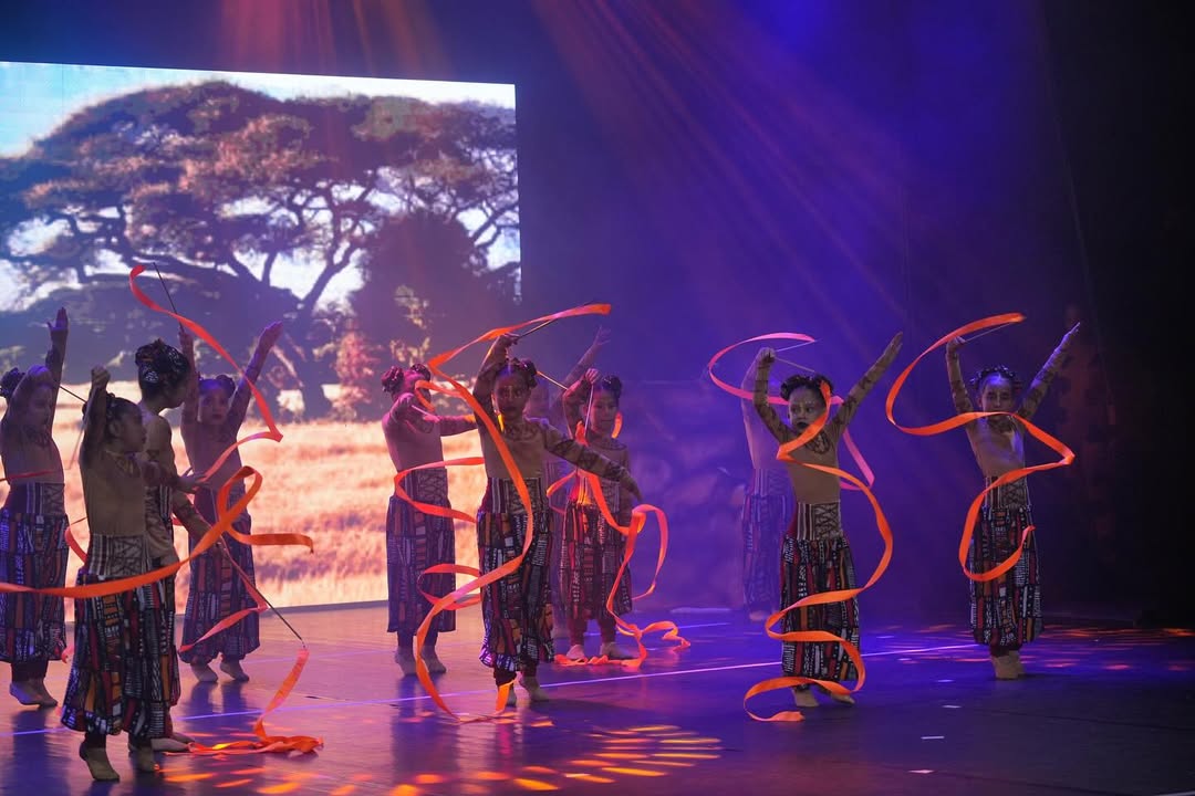 Bailarinos mirins com fitas laranja no espetáculo O Rei Leão