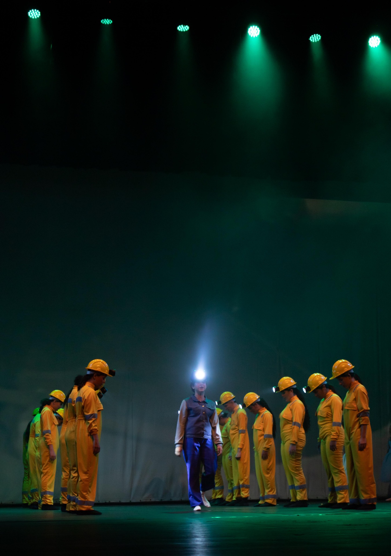 Mineiros enfileirados sob luz verde com lanternas no Billy Elliot