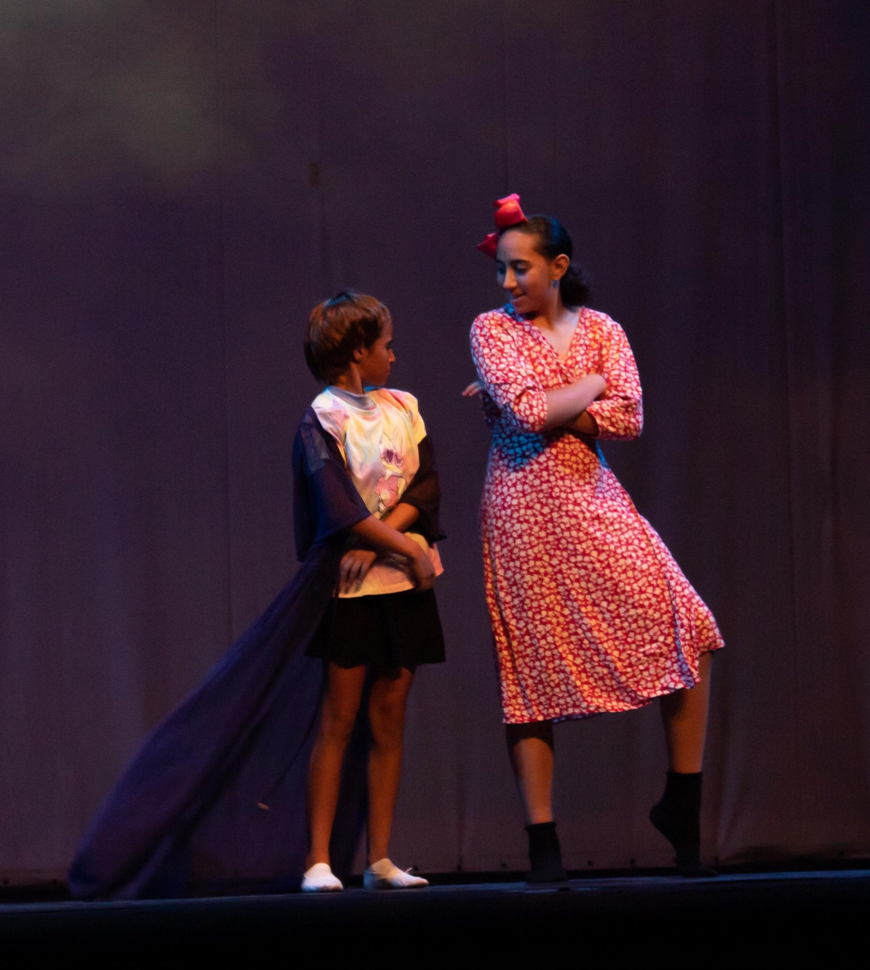 Billy ao lado de amiga com vestido vermelho e laço no espetáculo Billy Elliot